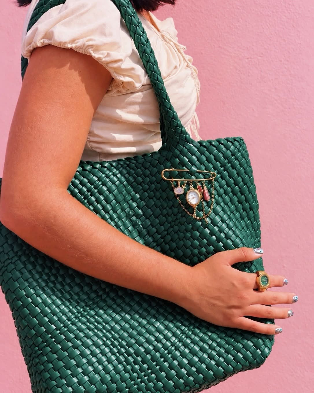 Client styling the EARTH PLUS FIRE La Isla Watch Brooch on a woven green bag