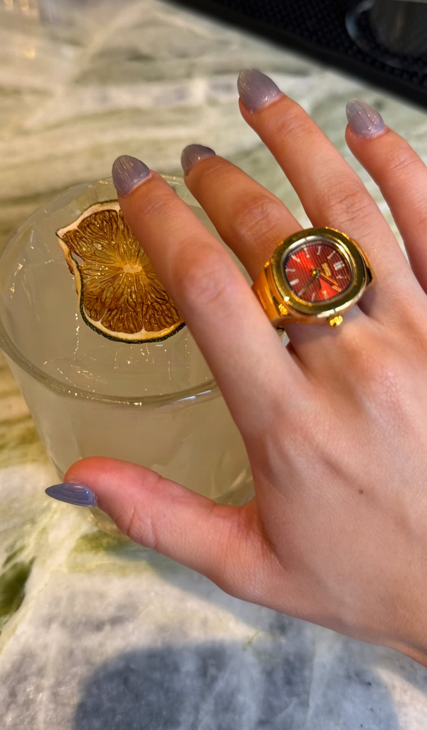 Client wearing a red-face EARTH PLUS FIRE watch ring while holding a citrus drink